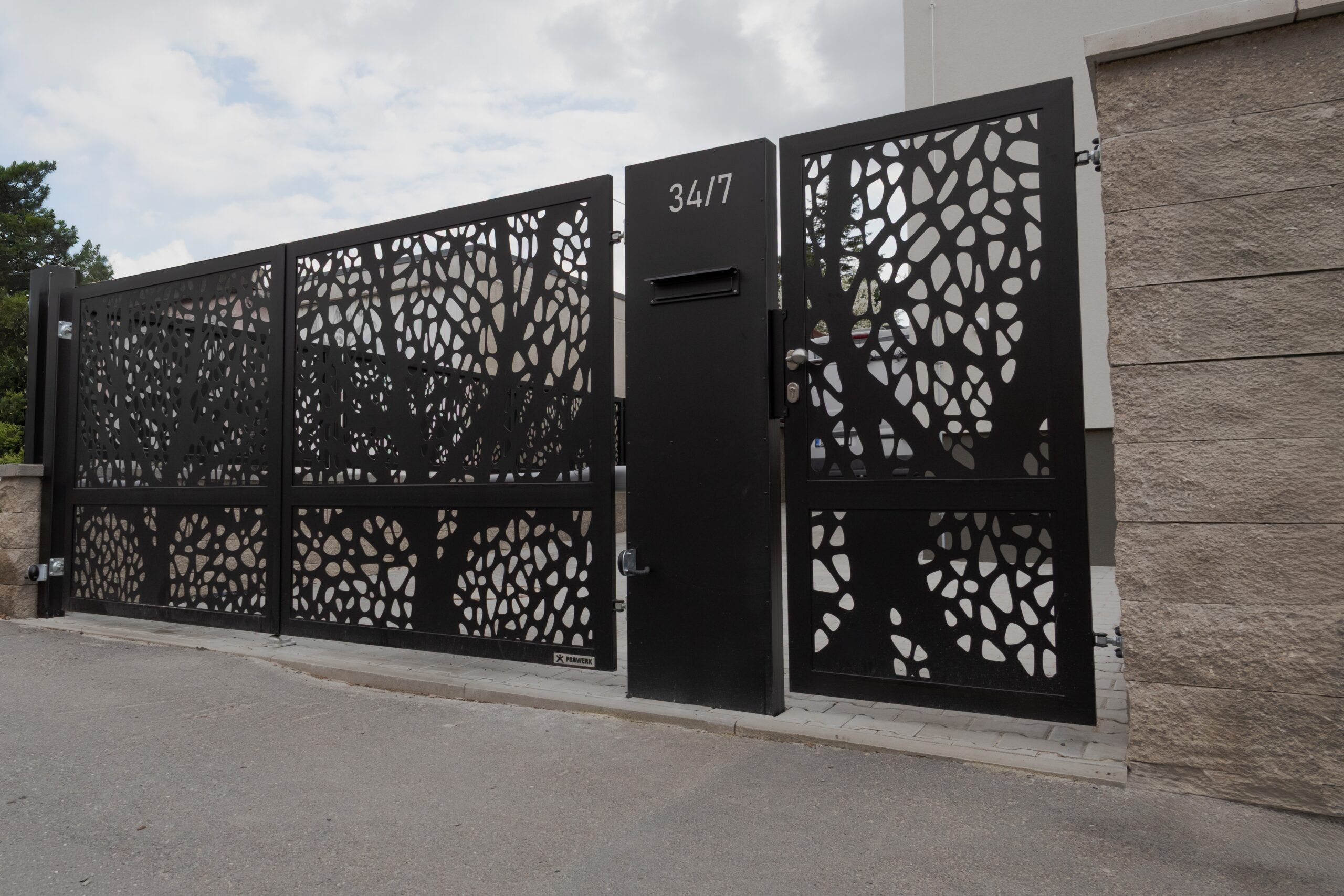 PROWERK vjezdová dvoukřídlá brána, funkční prostorový sloupek s integrovaným post boxem a vstupní branka. Design laserem vypálené siluety stromu IDENTITY PVDV07. Realizace Praha.