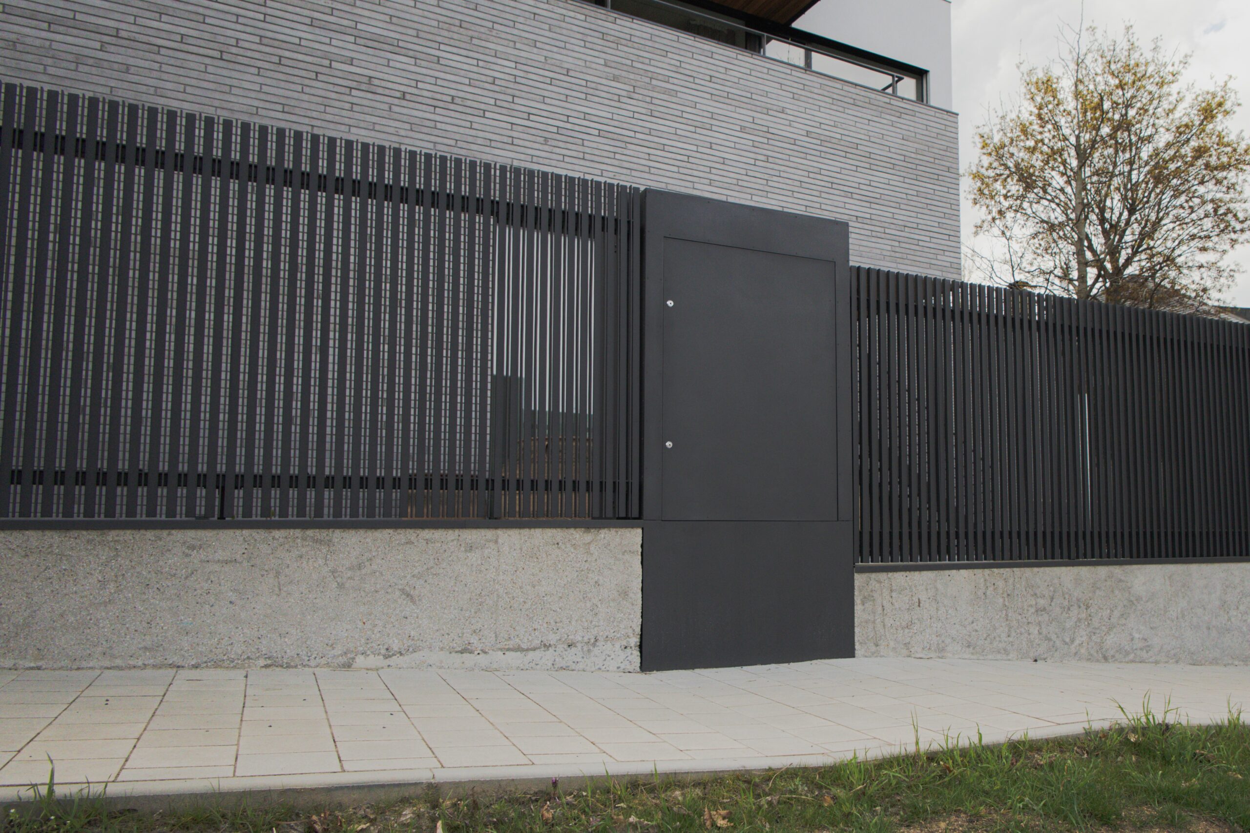 PROWERK exklusivní vstupní oplocení RD Praha. Součást oplocení plotová pole na betonové podezdívce v designu MIRAGE PV1602 se svislými předsazenými mikro-lamelami slícovanými s podezdívkou. Opláštění zděného pilířku v designu FORTIS PV1404 s plechovými 2D panely.