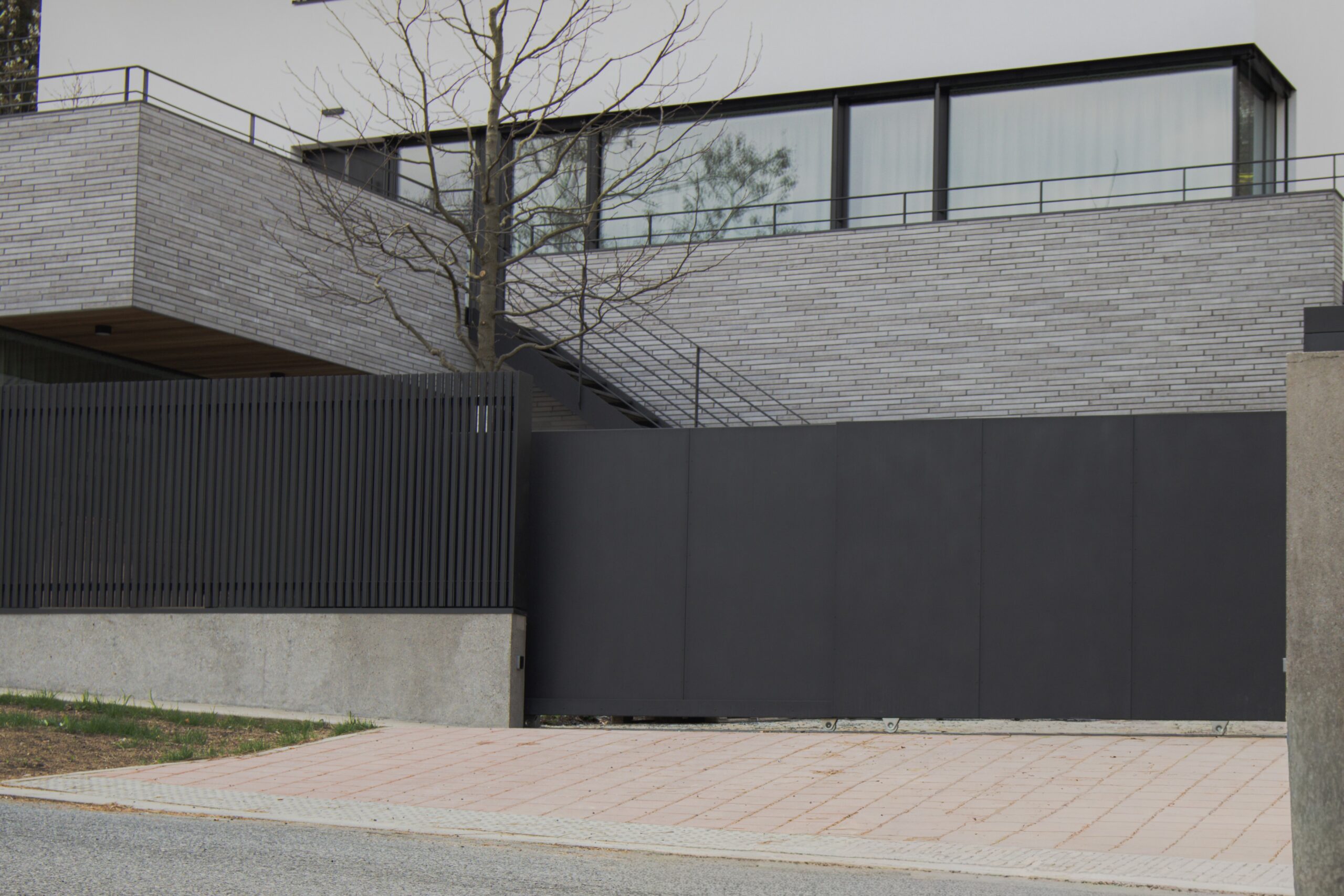 PROWERK dvoukřídlá pojezdová brána na kolejnici v designu plechových 2D panelů FORTIS PV1404. Plotové pole na betonové podezdívce designu MIRAGE PV1602 s mikrolamelami. Realizace Praha Barrandov.