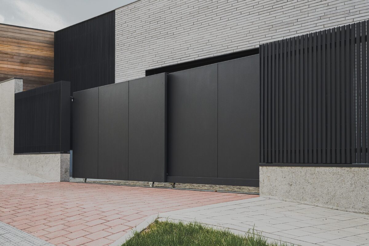 PROWERK exklusivní vstupní oplocení. Detail na teleskopickou pojezdovou bránu s výplní FORTIS 2D plechové panely PV1404, plotové pole slícované s podezdívkou designu MIRAGE PV1602. Ve stejném designu je provedená krycí stěna se vstupními dveřmi k technickému zázemí domu. Realizace Praha.