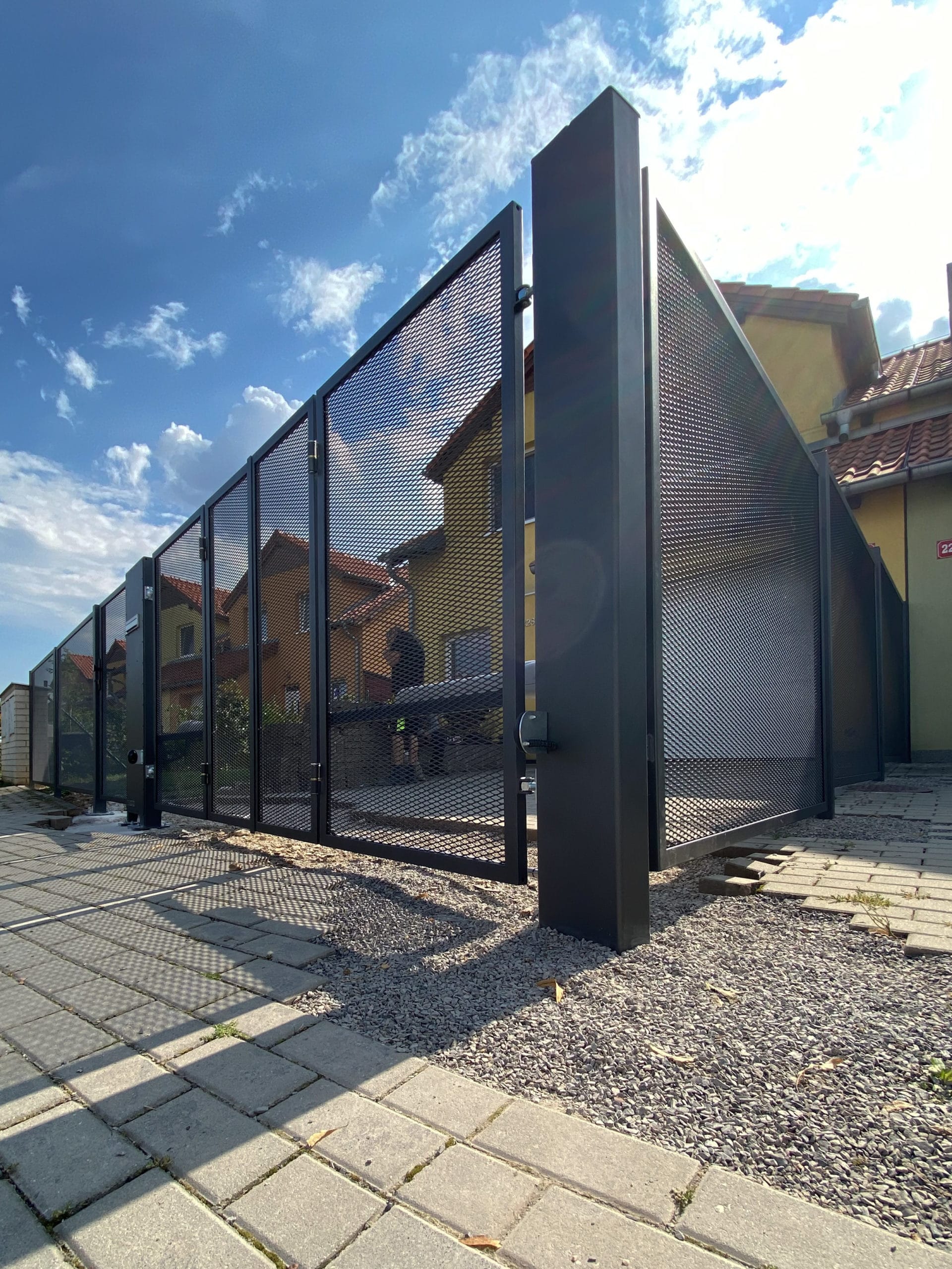 Skládací křídlová vjezdová brána v kovovém oplocení zhotoveném na míru s výplní tahokov. Součástí oplocení vstupní branka a prostorový sloupek. Realizace v Rudné u Prahy.