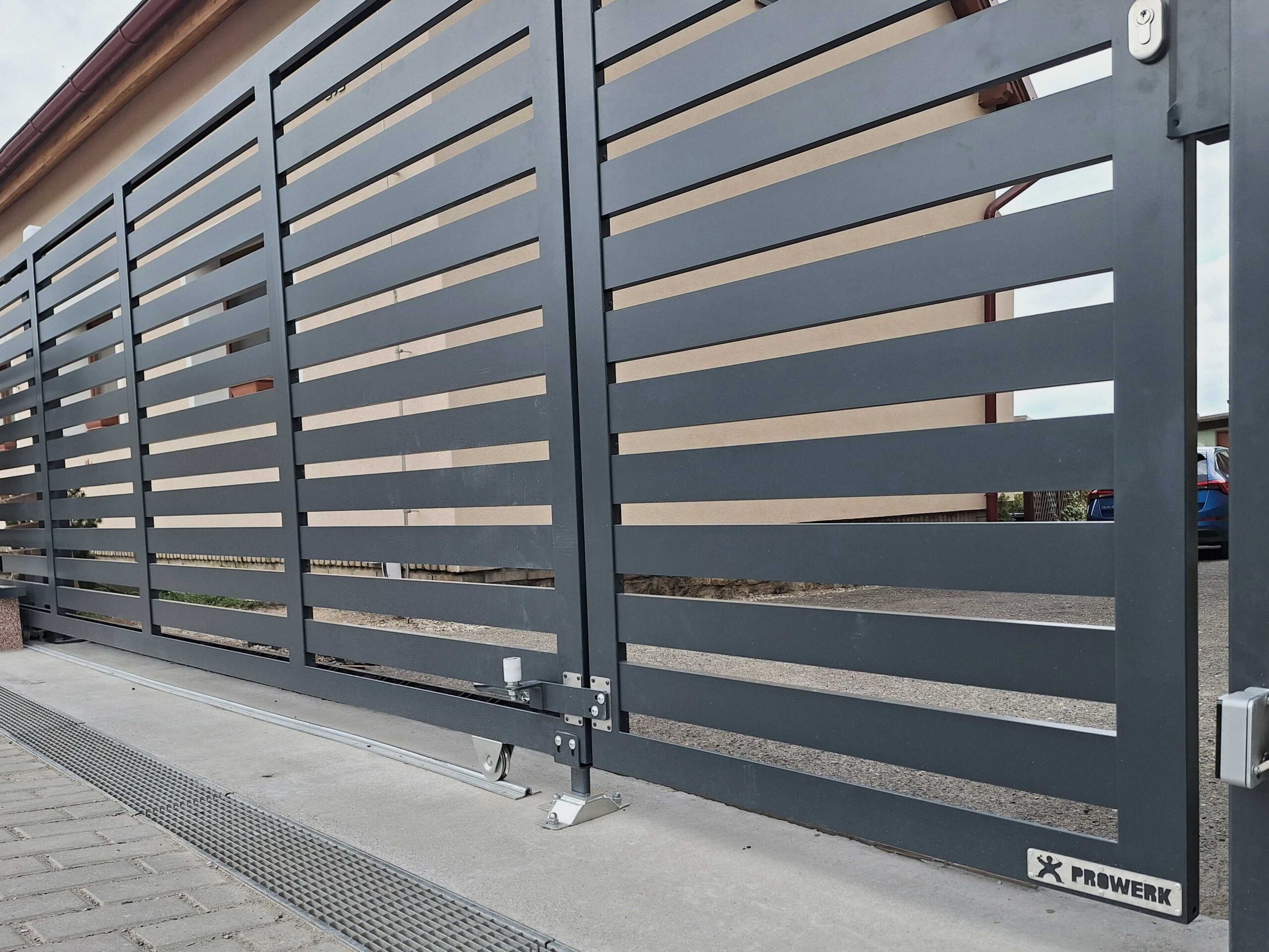 Pojezdová brána na kolejnici PROWERK s integrovanou brankou SYNERGY. Detail nájezdového trnu do spodní kapsy a vyklápěcí kladky branky.